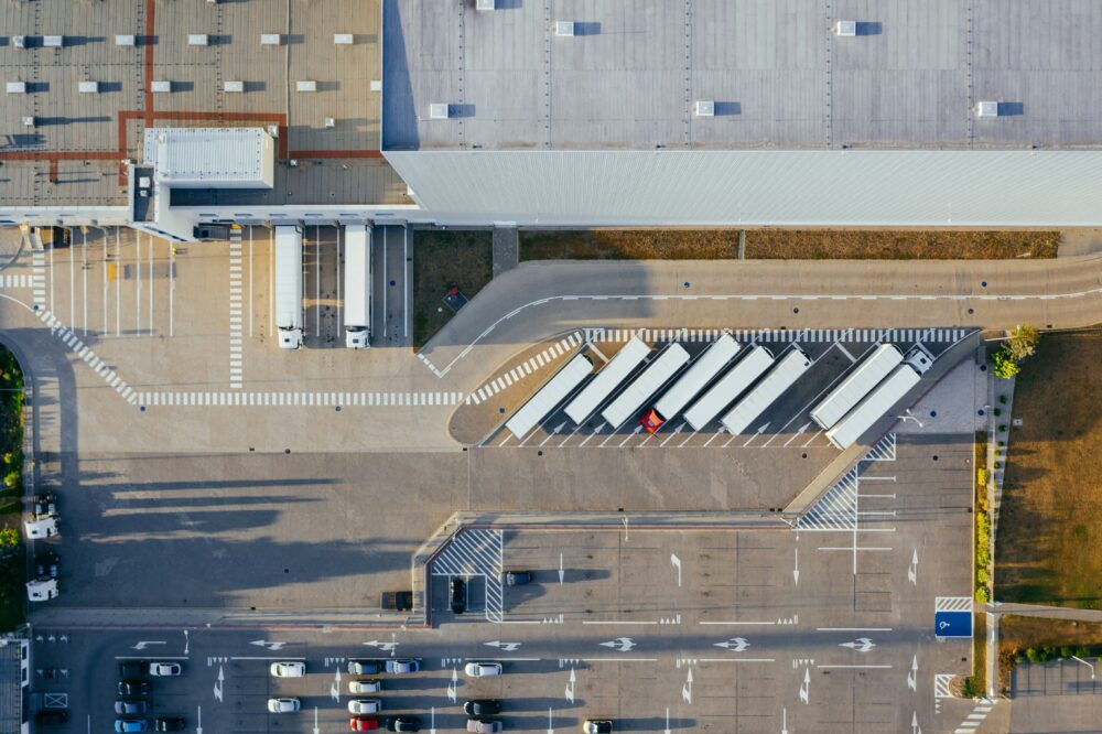 Ein Parkplatz fotografiert aus der Vogelperspektive, auf dem mehrere Lastwägen nebeneinander stehen und ein geometrisches Muster erzeugen